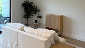 Un salon moderne avec une grande fenêtre, un canapé blanc, un meuble en bois et une plante en pot.