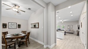 Uma sala de jantar ampla com uma mesa e cadeiras de madeira, um ventilador de teto e decoração nas paredes.