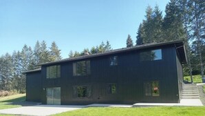 A modern two-story building with large windows and a flat roof, surrounded by a grassy area and trees.