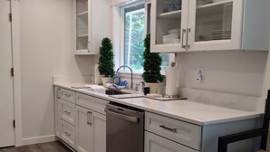 A modern kitchen with white cabinetry, a built-in dishwasher, and a window providing natural light.