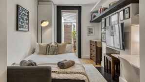 A modern bedroom with a bed, bedside lamp, dresser, and a TV on a wall.