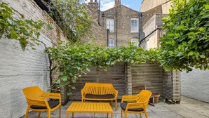 A patio with yellow chairs and a table, surrounded by brick walls and greenery.
