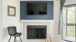 En moderne stue med et fladskærms-tv monteret på en blå væg med små prikker, en pejs nedenunder, en sort læderstol og et træbord.