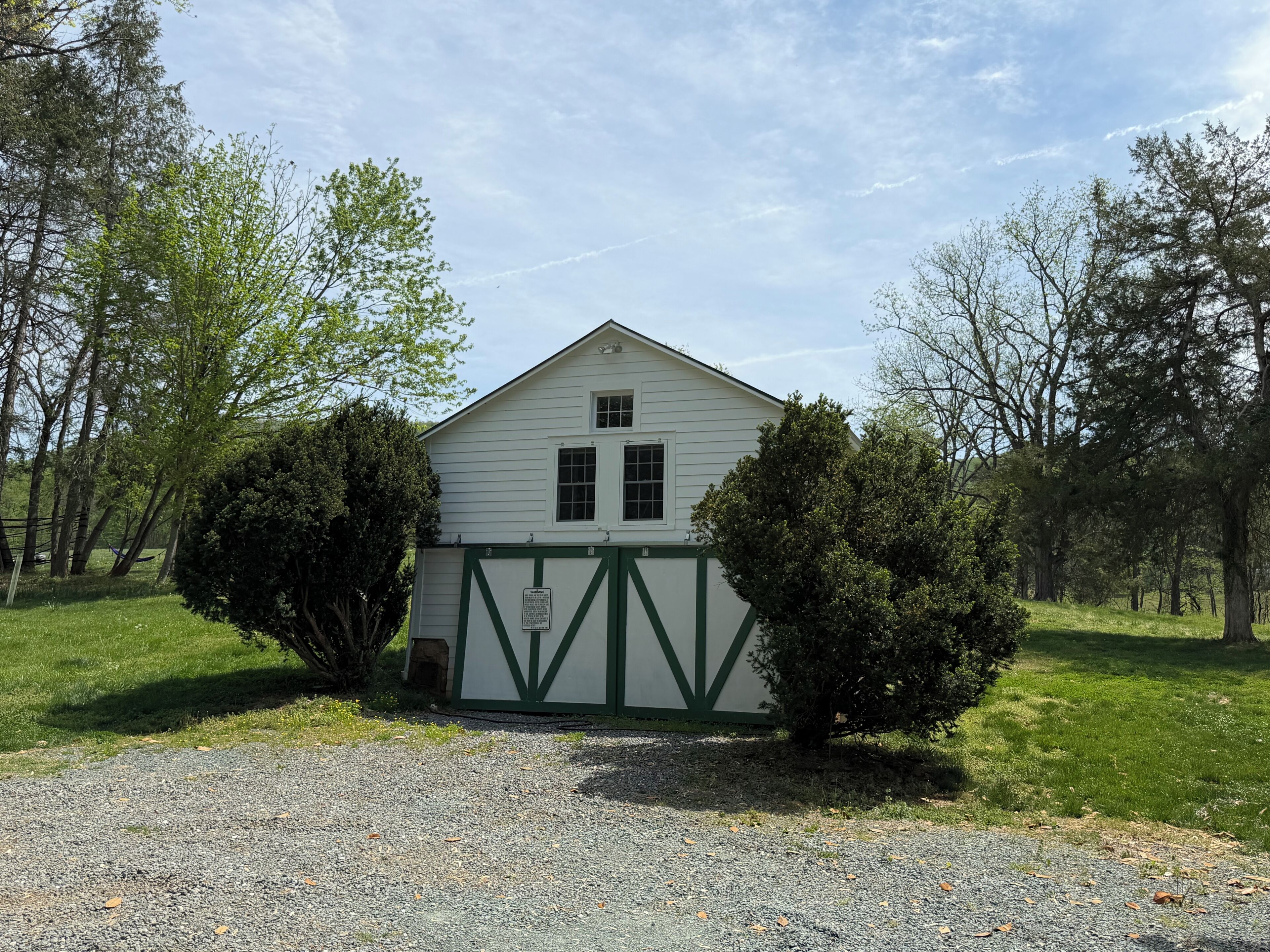 A white building with a green gate, surrounded by trees and grass.