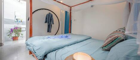 Un dormitorio con cama a dosel, perchero colgante, lámpara de noche y vista al baño.