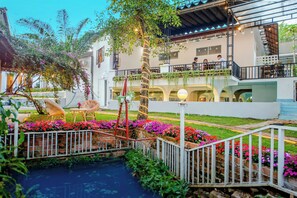 A hotel with a garden area featuring a small pond, outdoor seating, and a balcony with plants. - Homestay Vuon Phap BMT (Buon Ma Thuot)