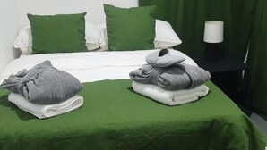 Una cama bien hecha con ropa de cama verde y blanca, una toalla gris y una toalla enrollada sobre una almohada blanca.