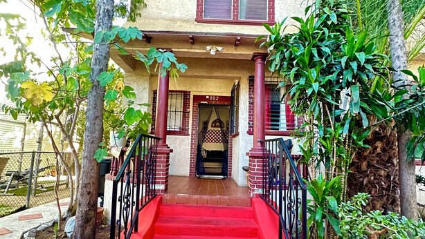Un edificio de dos pisos con fachada roja, entrada de ladrillo y una escalera roja que conduce a la puerta.