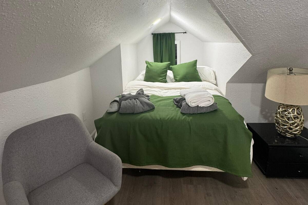 Ein kleines, dreieckiges Schlafzimmer im Dachgeschoss mit einem Bett, einem Stuhl und einem Nachttisch.