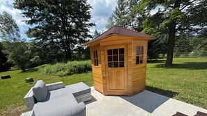 A small wooden structure with a door and windows, surrounded by a concrete patio with outdoor furniture.