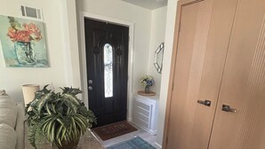 A hallway with a wooden door, a potted plant, a rug, and a painting on the wall.