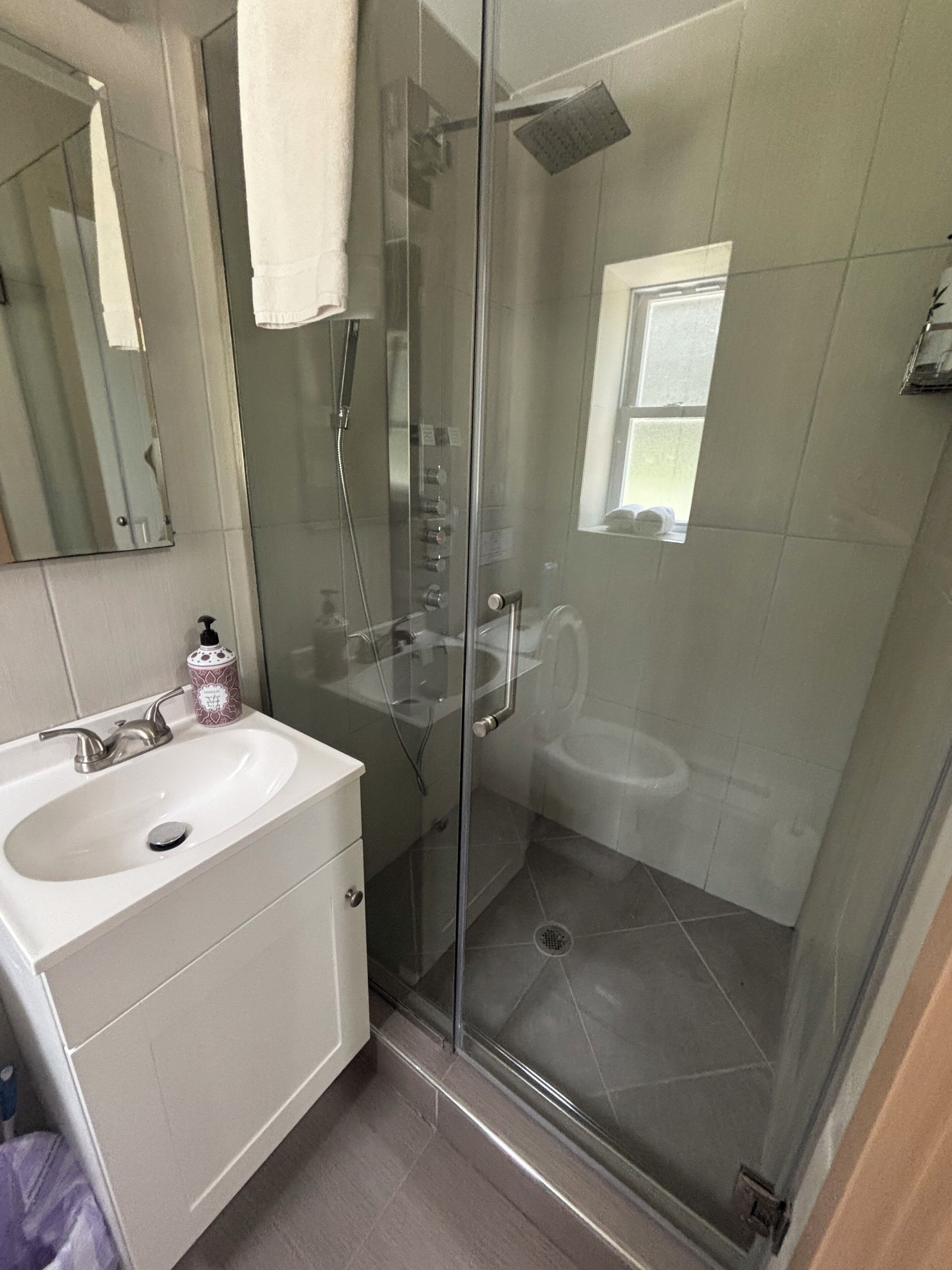 Une salle de bain moderne avec une douche à parois de verre, un lavabo blanc et un miroir.