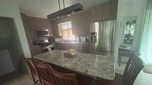 A modern kitchen with granite countertops, stainless steel appliances, and wooden chairs.