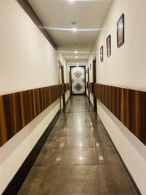 Un largo y estrecho pasillo con piso de mármol pulido, paneles de madera en las paredes y una serie de cuadros enmarcados a la derecha.