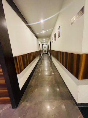 Un pasillo largo y estrecho con piso pulido, bordeado por paredes con estampado a rayas y un letrero que indica las habitaciones 201 a 204.