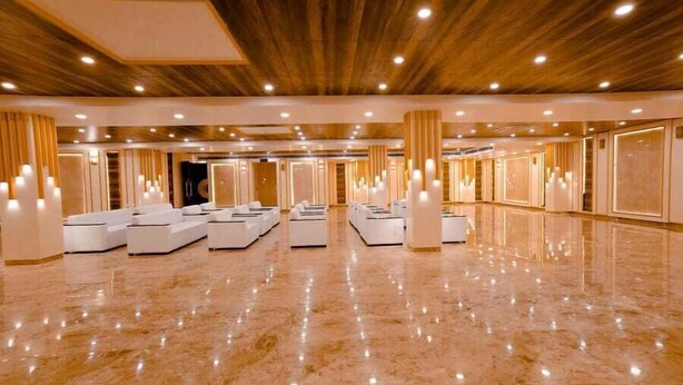 Un amplio vestíbulo de hotel con piso de mármol pulido, zonas de estar blancas y paneles de madera en el techo.