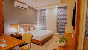 Habitación de hotel con cama, escritorio, silla, televisor y planta en maceta.