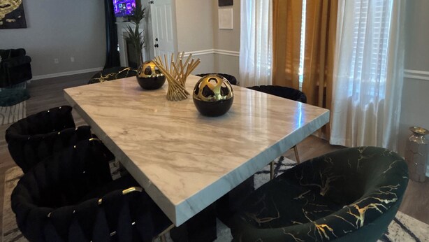 A dining area with a marble table, black chairs, a chandelier, and a television in the background. - The StayHaus, 
Relax in this stylish home! (Horn Lake)