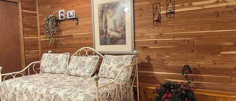 A bedroom with a wooden paneled wall, a bed with patterned bedding, a framed picture, and a potted plant.