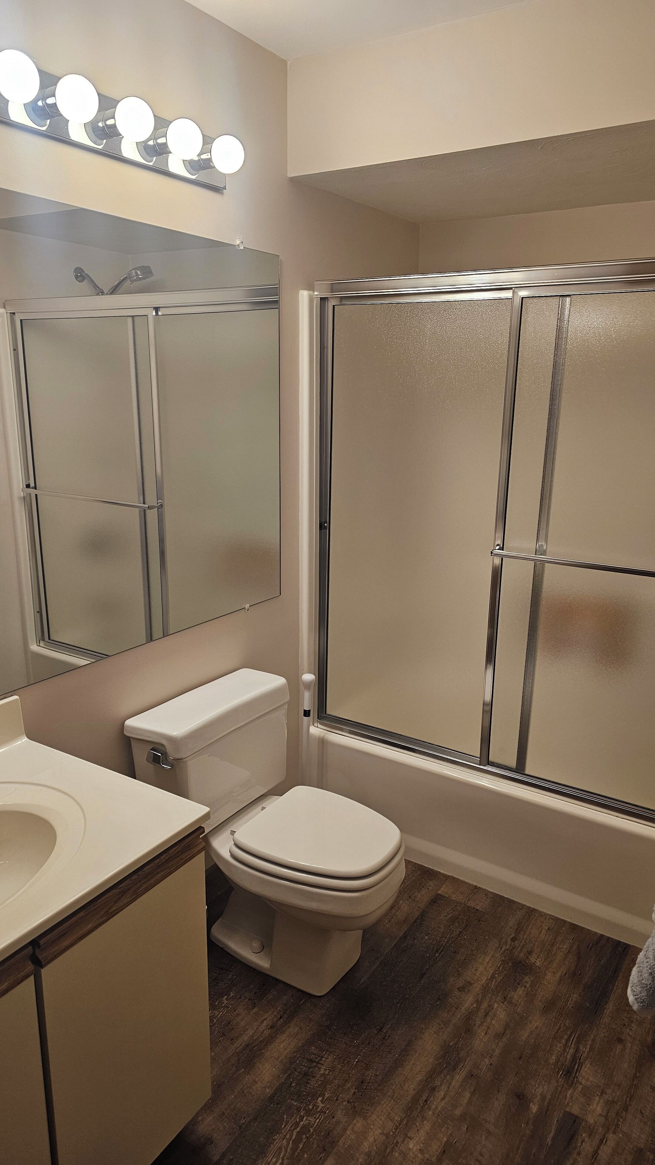 A bathroom with a toilet, sink, mirror, and glass shower enclosure.