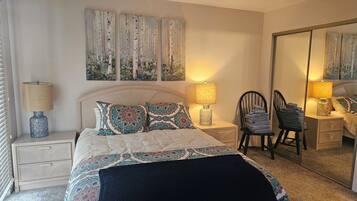 A bedroom with a bed, two bedside tables, a chair, a mirror, and wall art.