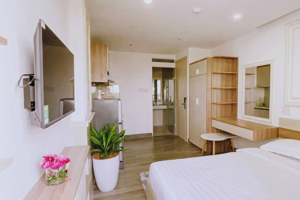 A modern hotel room with a bed, a TV mounted on the wall, a small table with a plant, and a wooden cabinet.