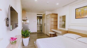 Une chambre d’hôtel moderne avec un lit, un téléviseur fixé au mur, une petite table avec une plante et une armoire en bois.