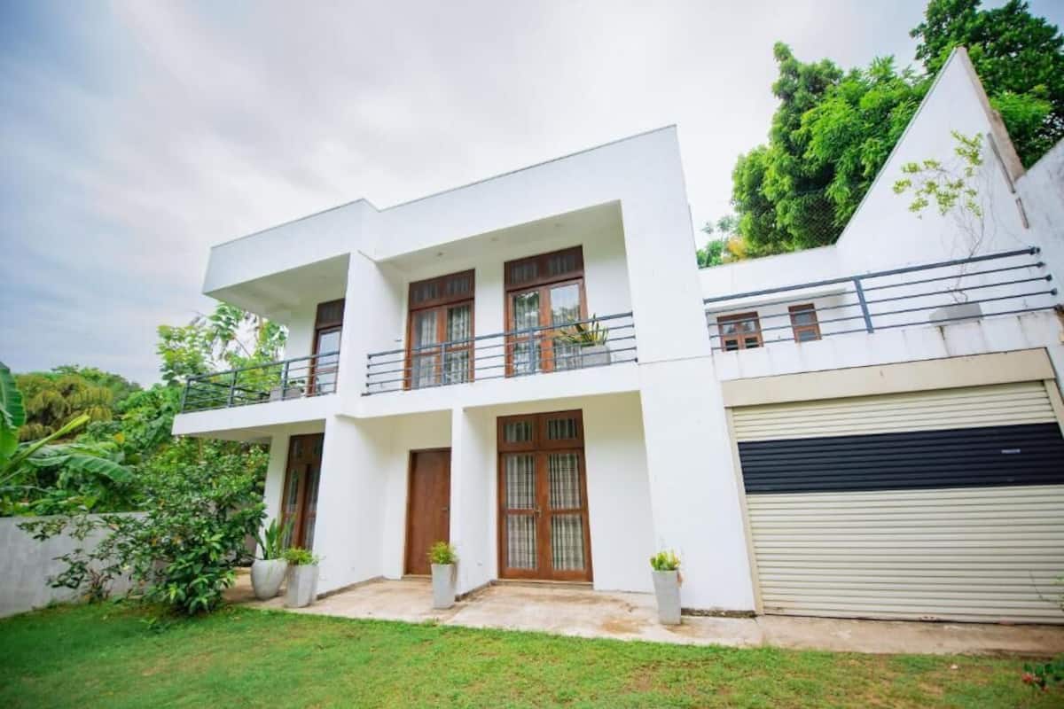 A modern two-story house with a flat roof, a balcony on the upper floor, and a garage with a roller door.