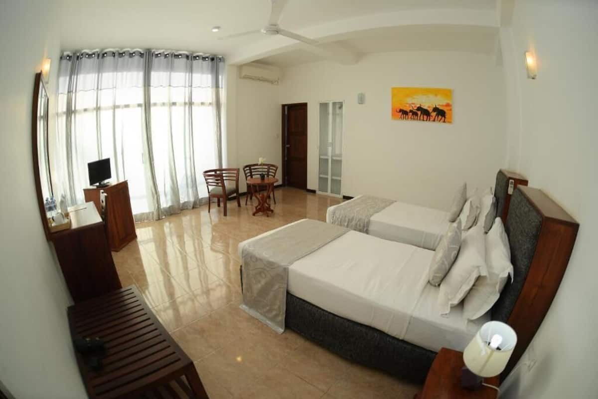 A hotel room with two beds, a desk, a chair, a TV, and a painting on the wall.