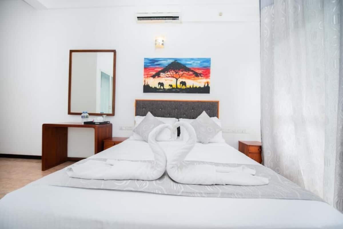 A hotel room with a bed, a bedside table, a mirror, and a painting on the wall.