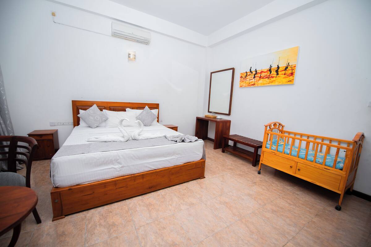 A bedroom with a wooden bed, a wooden crib, a nightstand, a chair, and a painting on the wall.