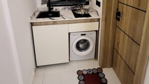 A compact kitchen with a built-in washing machine, a stove, and a cabinet with utensils. - Cozy Modern Studio Apartment in Ikoyi (Lagos)