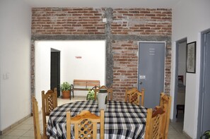 Zona pranzo con parete in mattoni, una panca, piante in vaso e tovaglia a quadri.