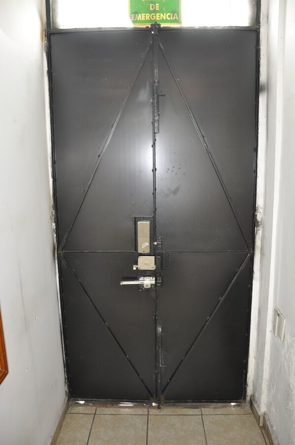 Una porta in metallo nero chiusa con un cartello sopra che riporta la scritta 'EMERGENCIA' (emergenza).