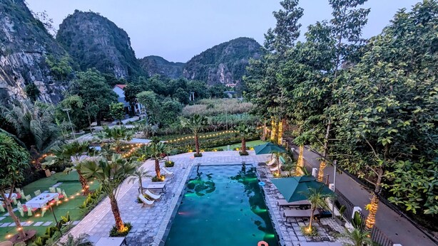 Piscina com espreguiçadeiras e guarda-sóis, cercada por vegetação e montanhas.