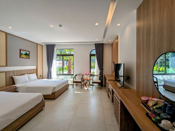 A hotel room with two beds, a desk with a TV, and a view of greenery outside.
