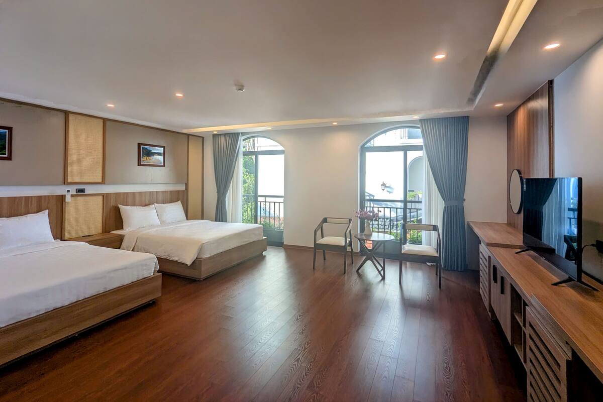 A hotel room with two beds, a TV, a small table with flowers, and a balcony with a view.
