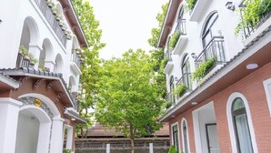 Pátio com uma árvore central, rodeado por edifícios com varandas e janelas em arco.