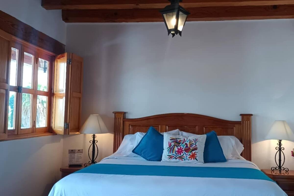 Une chambre à coucher avec un lit en bois, deux tables de chevet avec des lampes, une fenêtre avec des cadres en bois et un luminaire suspendu.