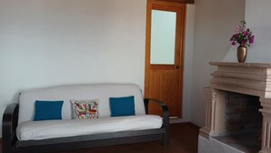 Un sofá blanco con cojines azules, una puerta de madera y una chimenea con un florero.