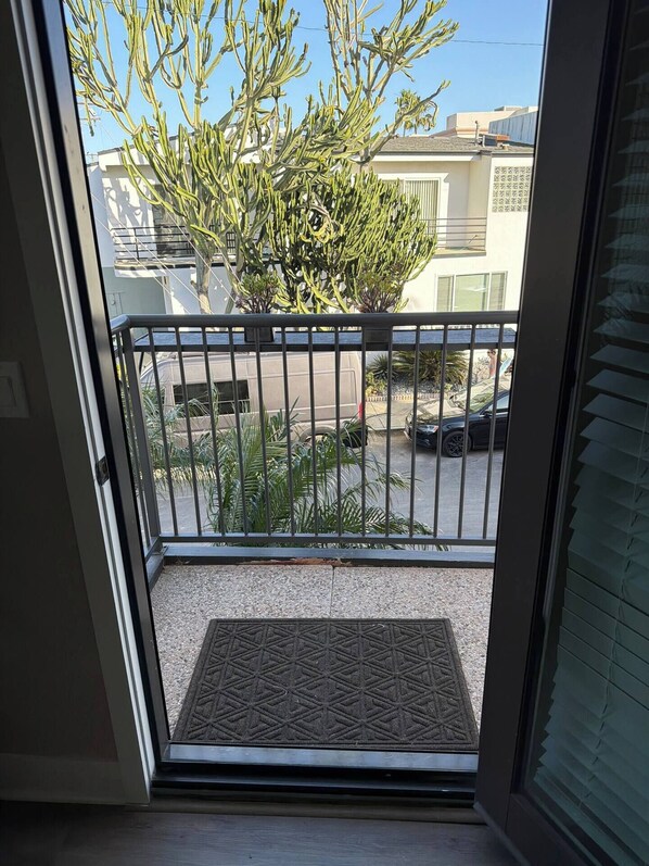 Une vue depuis un balcon doté d’une rambarde en métal, d’un paillasson et d’un petit espace jardin agrémenté de diverses plantes.