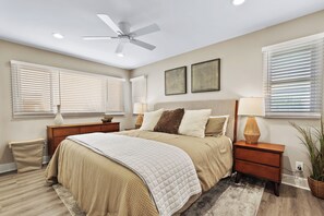 A bedroom with a bed, nightstands, a ceiling fan, and wall-mounted artwork.