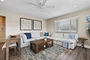 A modern living room with a sectional sofa, a wooden coffee table, a decorative rug, and a ceiling fan.