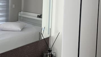 A modern hotel room with a bed, a nightstand, a mirror, and a window with blinds.