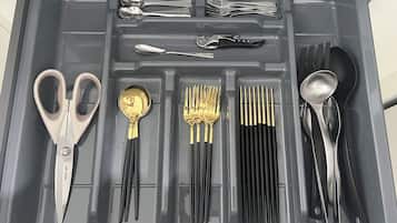 A drawer containing various utensils and cutlery, including forks, spoons, and a pair of scissors.
