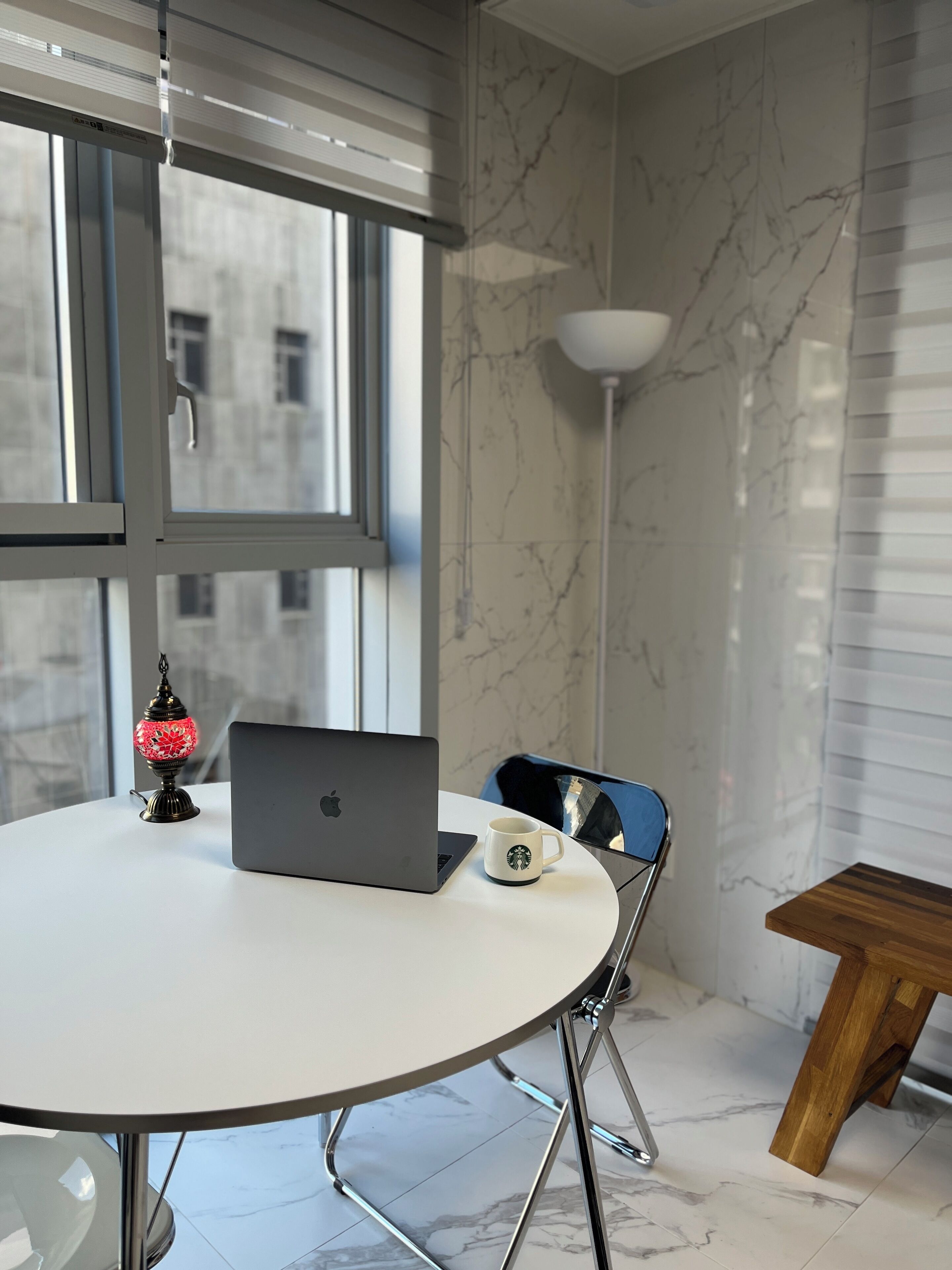 A modern room with a round table, a laptop, a Starbucks mug, and a decorative lamp.