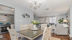 A modern kitchen with a dining area, a gray couch, and a chandelier. - Charming 3-bedroom Pool House with WiFi and AC in Palm Bay (Palm Bay)