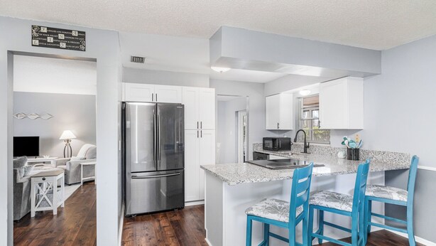 A modern kitchen with white cabinets, a stainless steel refrigerator, and a granite countertop. - Charming 3-bedroom Pool House with WiFi and AC in Palm Bay (Palm Bay)