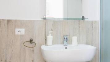 A bathroom with a white sink, a glass shelf above it, and a wooden wall.