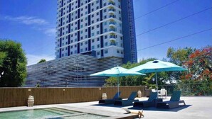 Un immeuble de grande hauteur au design moderne, doté d’une piscine et de chaises longues extérieures avec parasols.